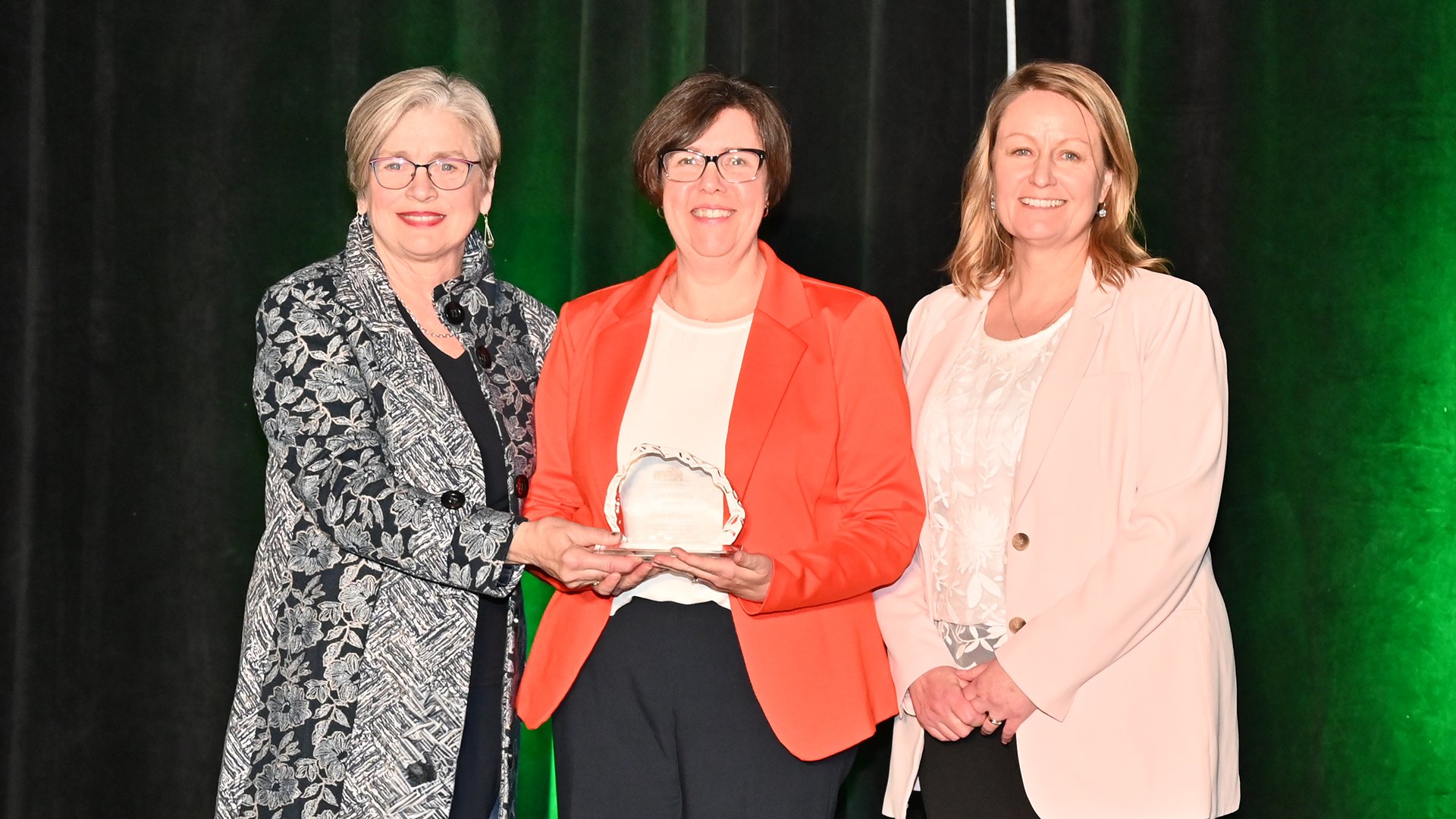 Three women stand on stage holding an award