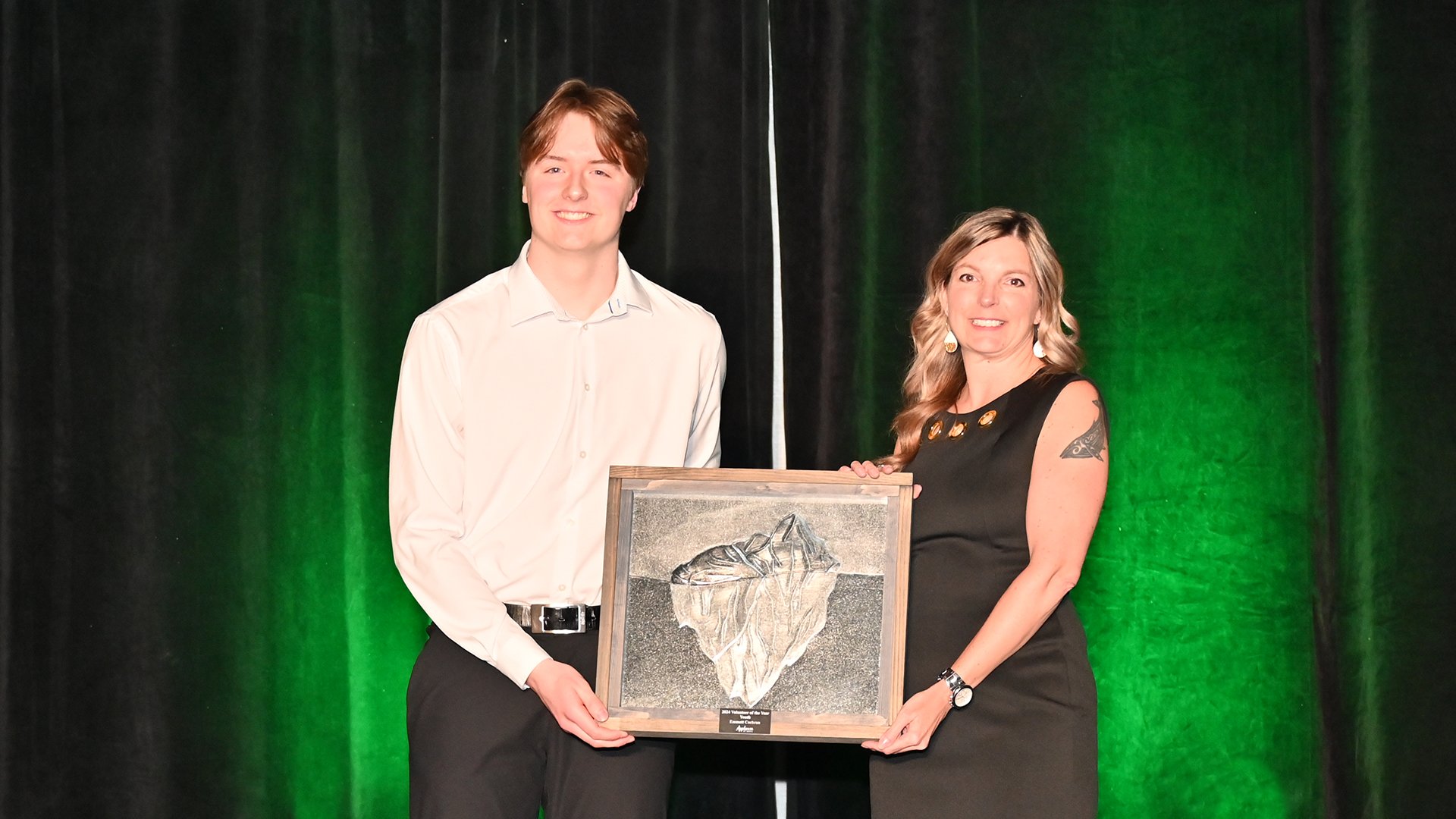 A man and woman stand on stage holding an award