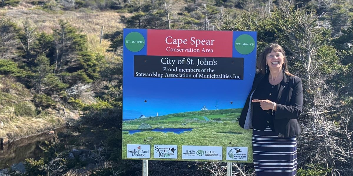 Deputy Mayor Sheilagh O'Leary standing with a new conservation area sign installed in Cape Spear that states 
