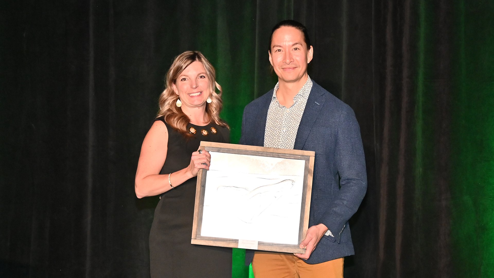 A woman and a man stand on stage holding an award