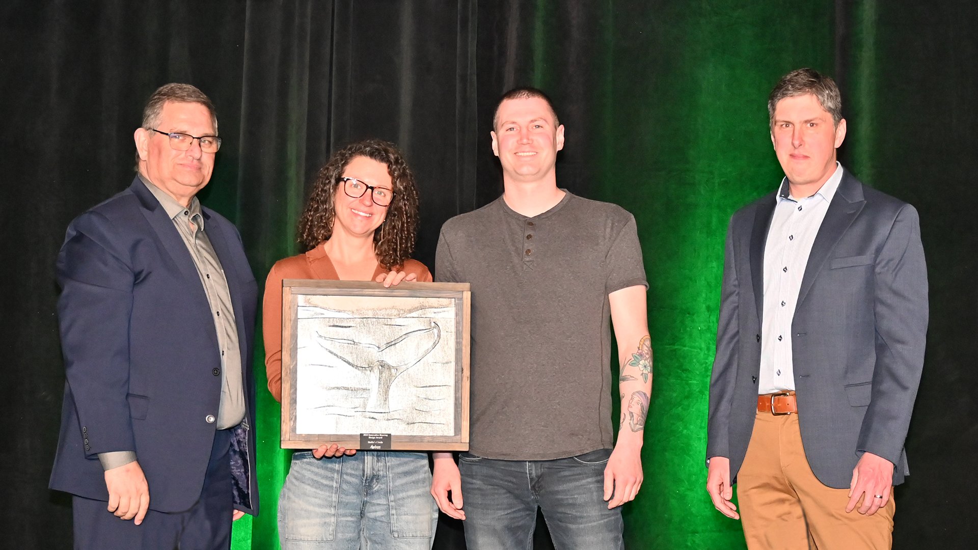 Three men and a woman stand on stage, woman is holding an award