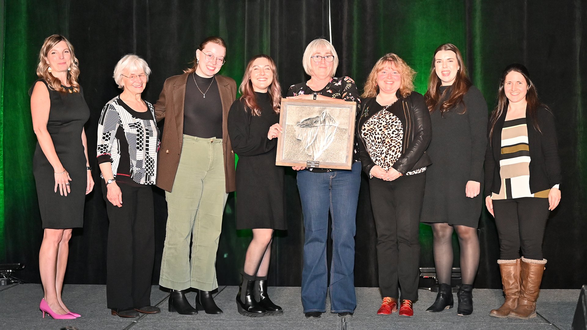 Eight women stand on stage, one holds an award