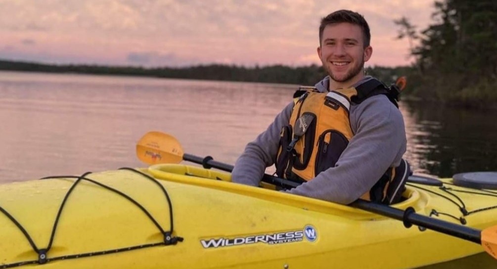 Morgan Cole smiling at camera in a kayak as the sun sets in the background