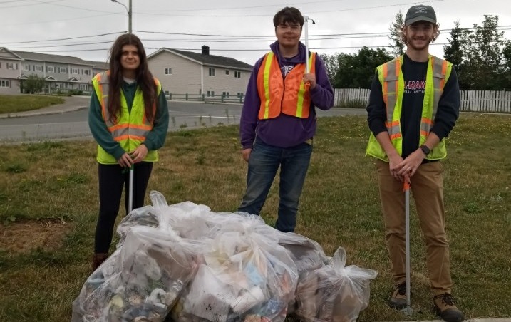 three individuals smile at the camera in front of large bags of garbage