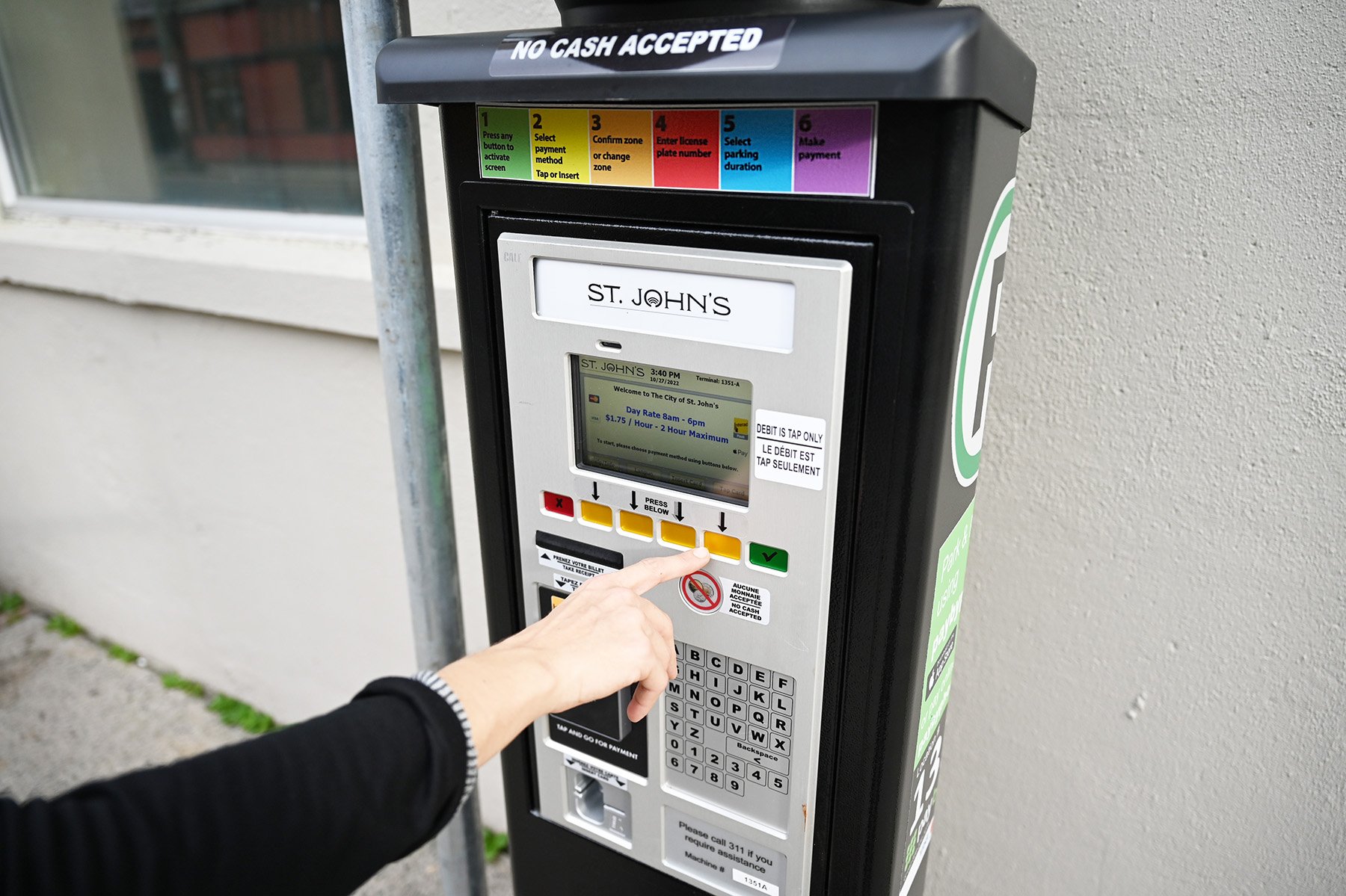 A person's hand is reaching out to press a button on a parking pay station.