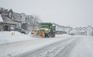 snow covered street view with a green snow plow