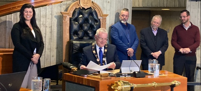 individuals surround Mayor Breen in Council Chambers as he signs the proclamation