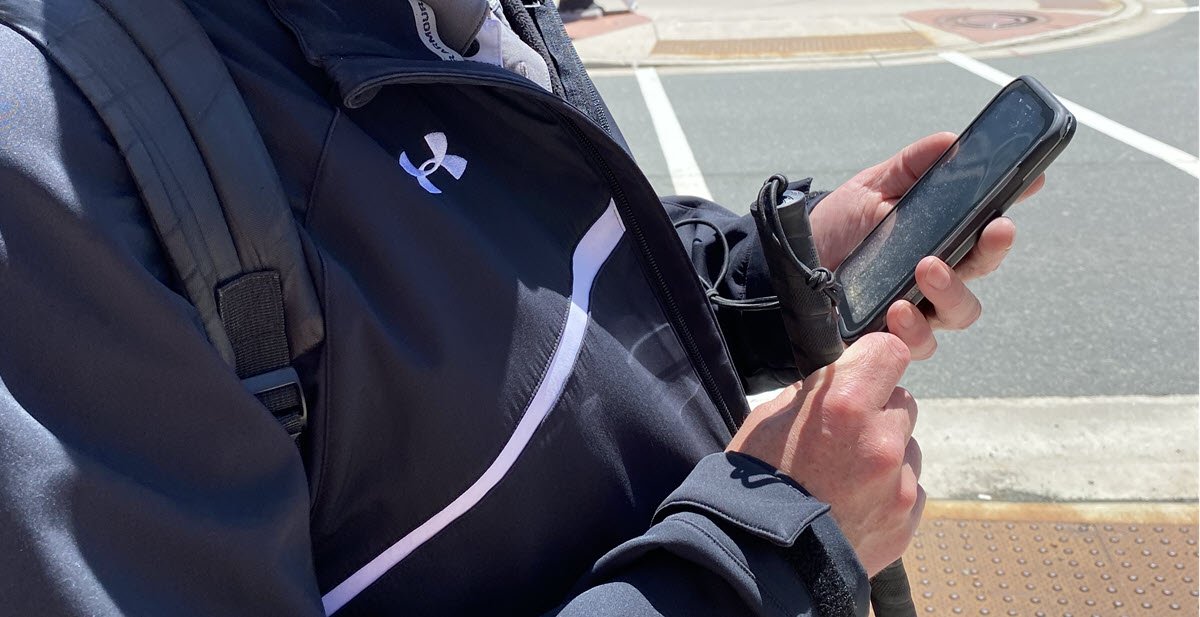 image of individual holding a cellphone and a walking stick standing on the street