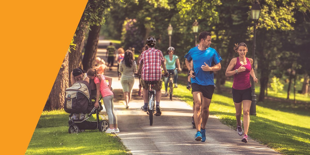 People running, walking and cycling on a shared use path, with a tree and green grass in the background.