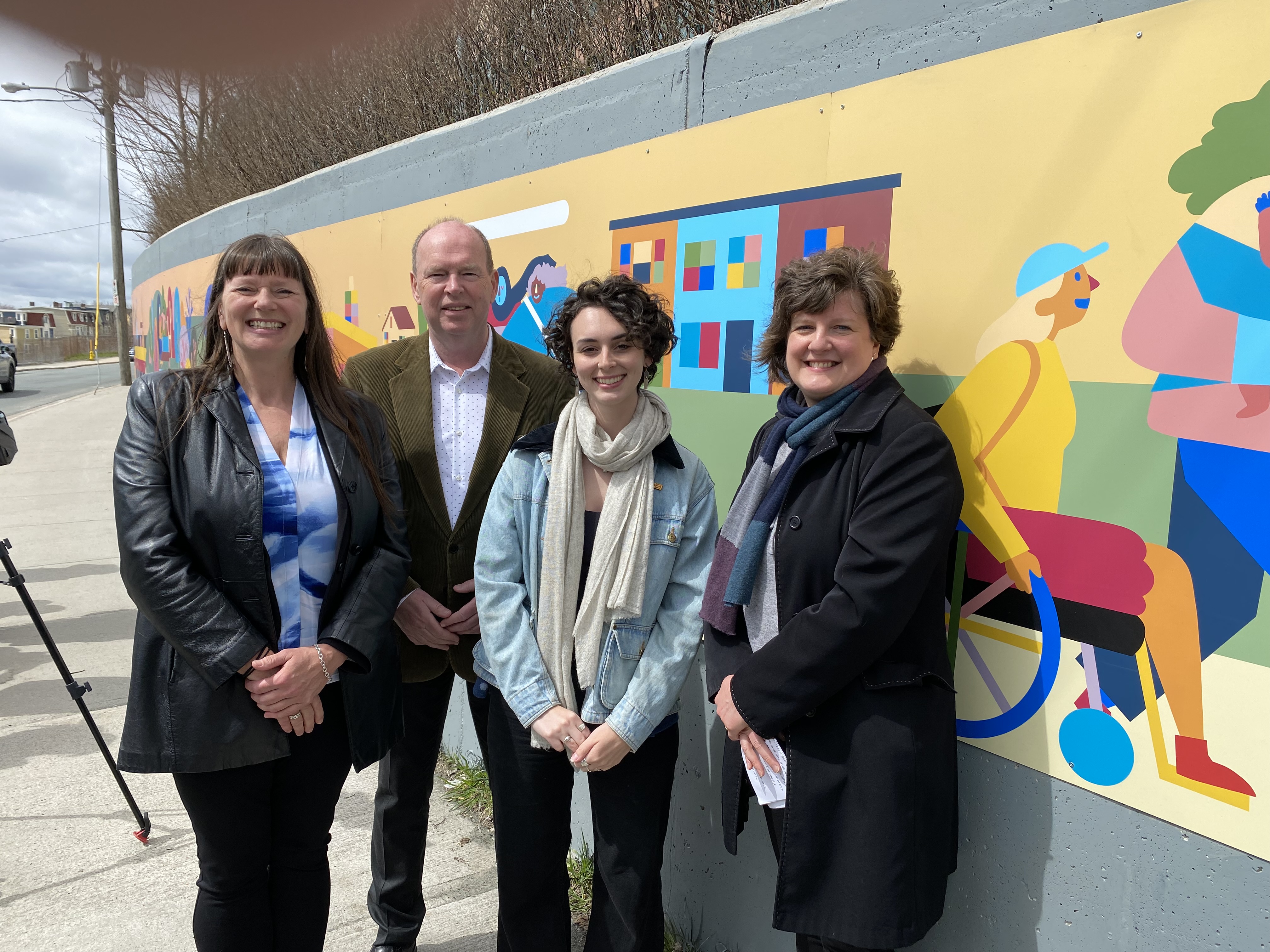 Four people stand in front of a colourful mural on harvey road.