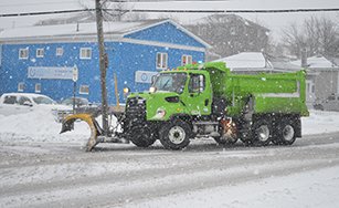Blue building with snow equipment driving by. 