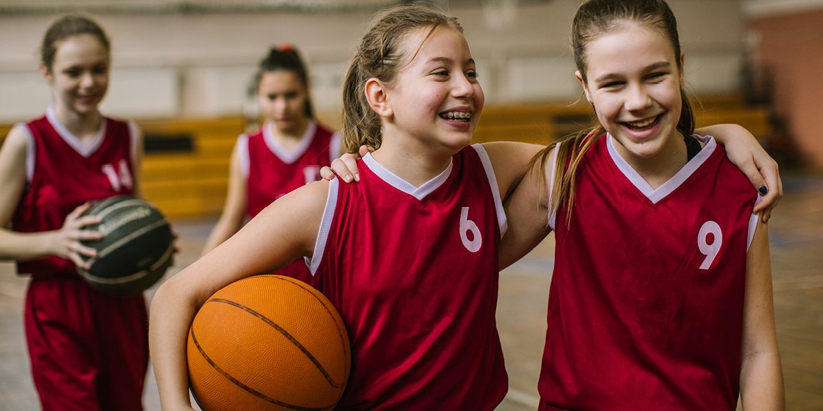 children smiling and wearing red uniforms with basketballs in their hands