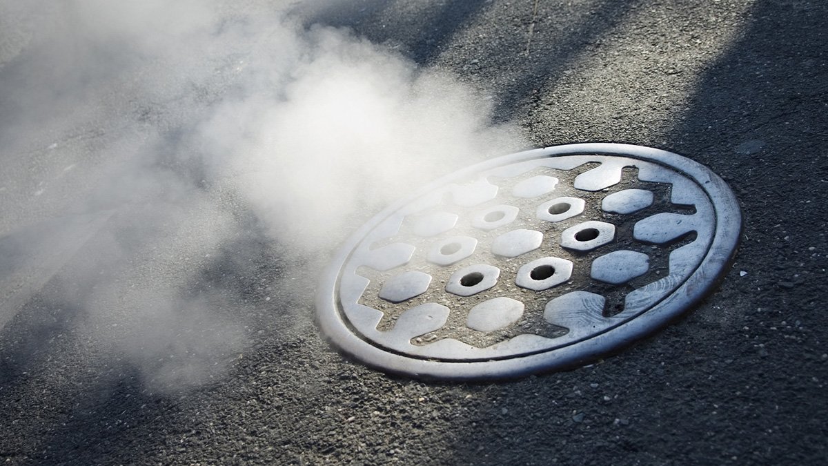round sewer cover in asphalt with vapour rising from below