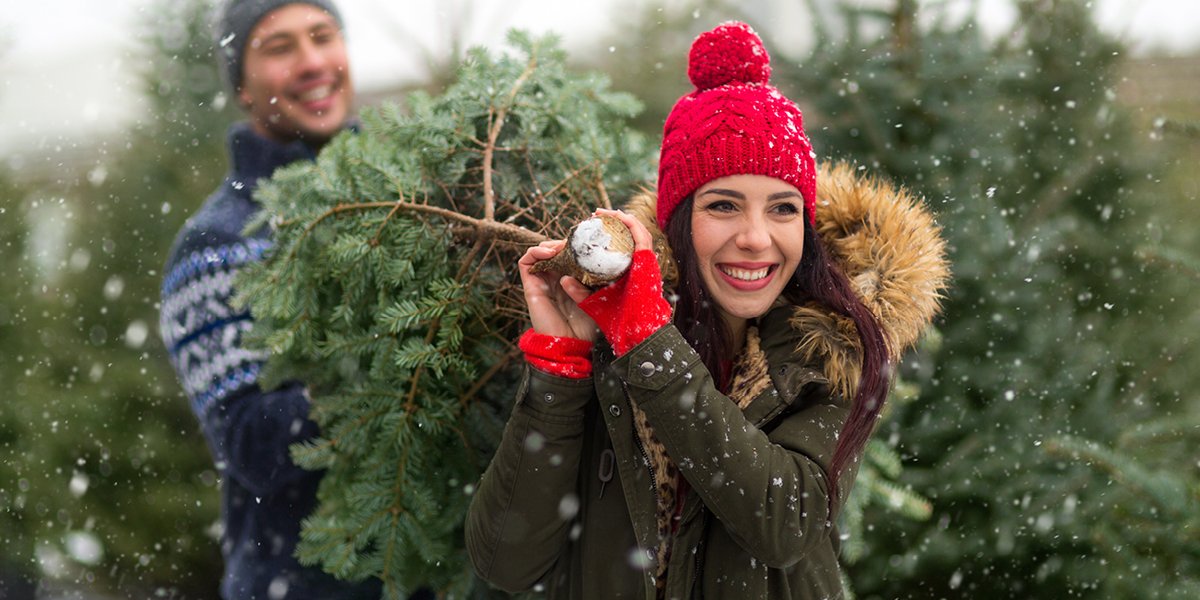 two people smiling and carrying a real Christmas tree. 