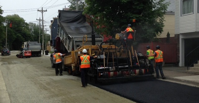 Paver with crew walking behind and fresh pavement over stone