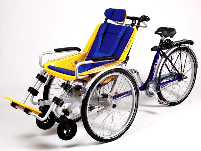 A Duet Bike, a three wheeled bicycle with two wheels in the front and a wheelchair type seat between them and with one wheel at the rear with a bicycle seat and handle bars for the person controlling the bicycle