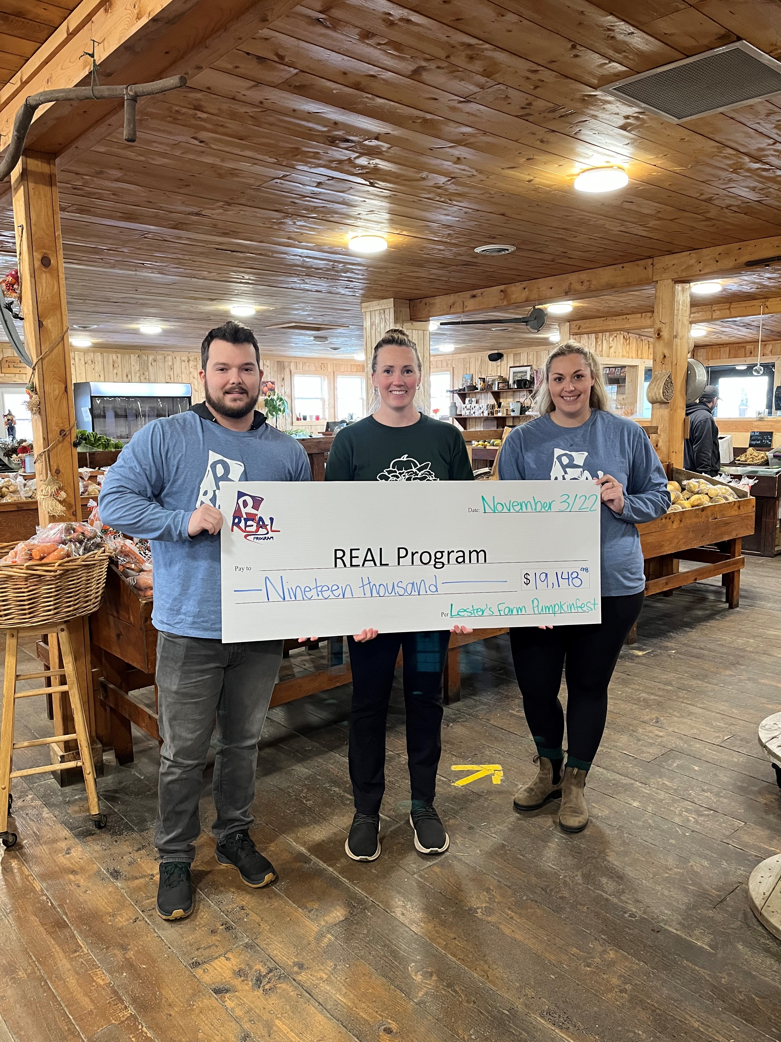 Two representatives of the REAL program and a representative from Lester's Farm holding a cheque for over 19,000 dollars