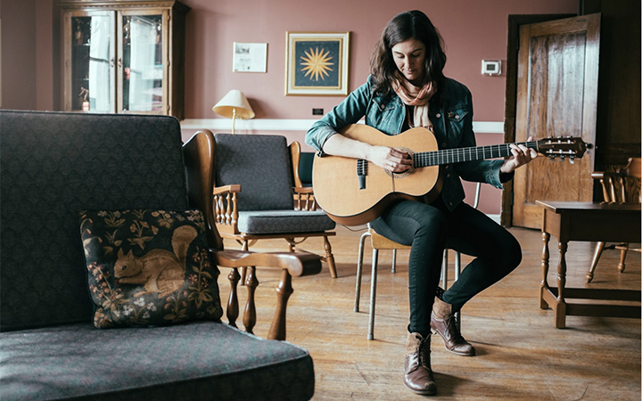 Kattie Baggs seated on a chair and playing guitar