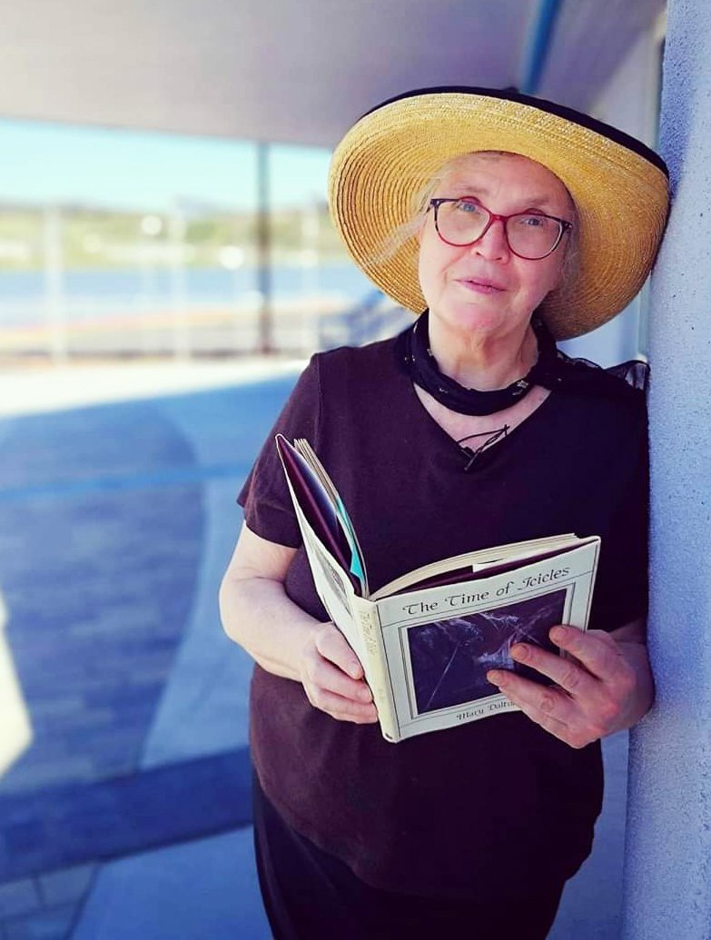 Poet Laureate stood leaning against a wall reading a book of poetry