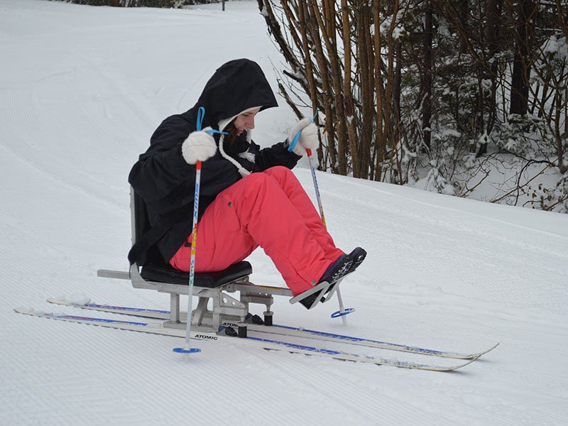 A woman in a sit ski, a chair mounted on two skis with a support for your feet and two poles used with your hands to move the equipment