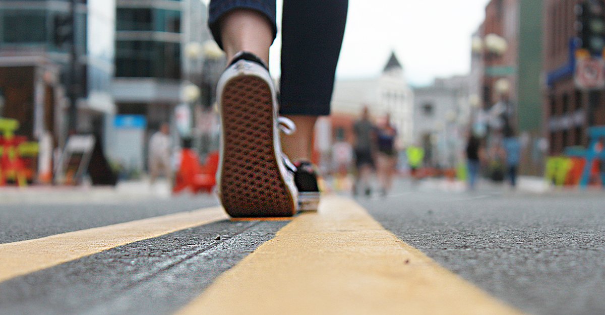 tight shot of a person's feet in sneakers walking on the double yellow line down the middle of Water Street