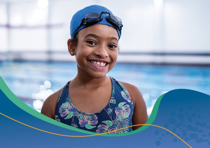 Child wearing a swim cap, smiling and standing next to a pool. 