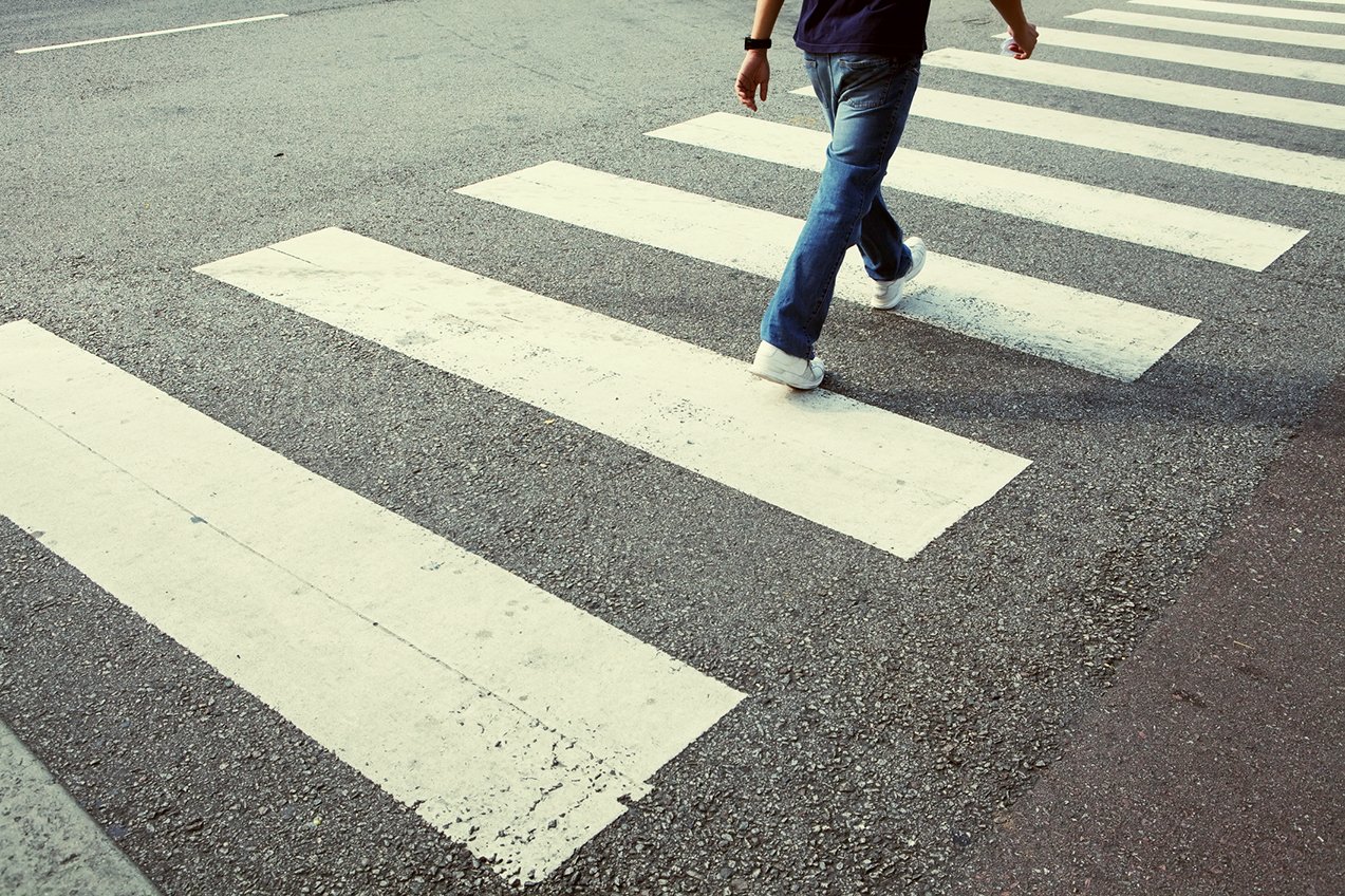 A man wearing jeans crosses the street at a crosswalk