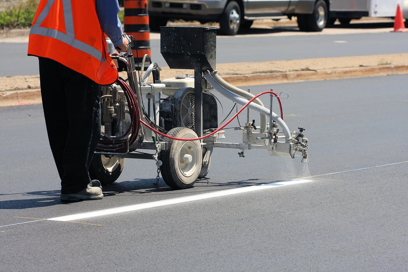 A person uses a machine to paint white lines on asphalt surface of road