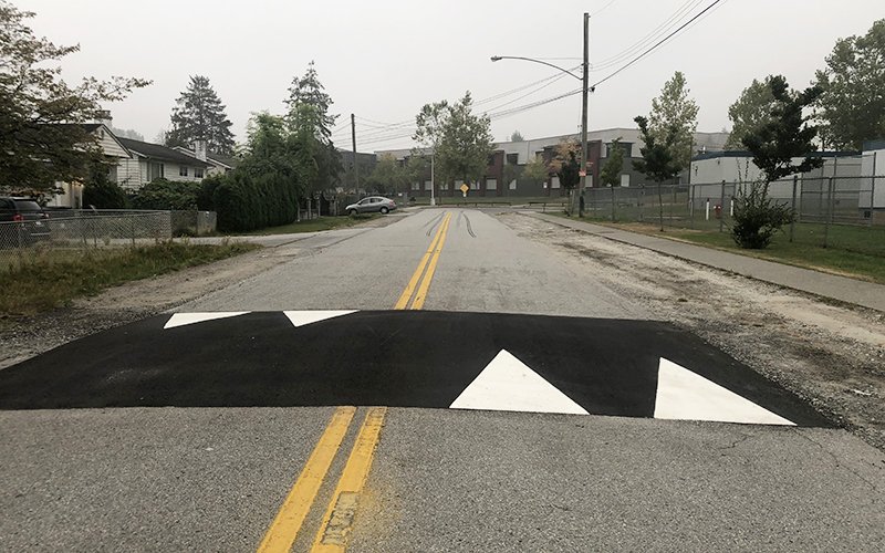 A raised hump of asphalt that spans the entire width of road for the two lanes that travel in both directions. The hump is marked with triangle white arrow pointers that show direction of travel