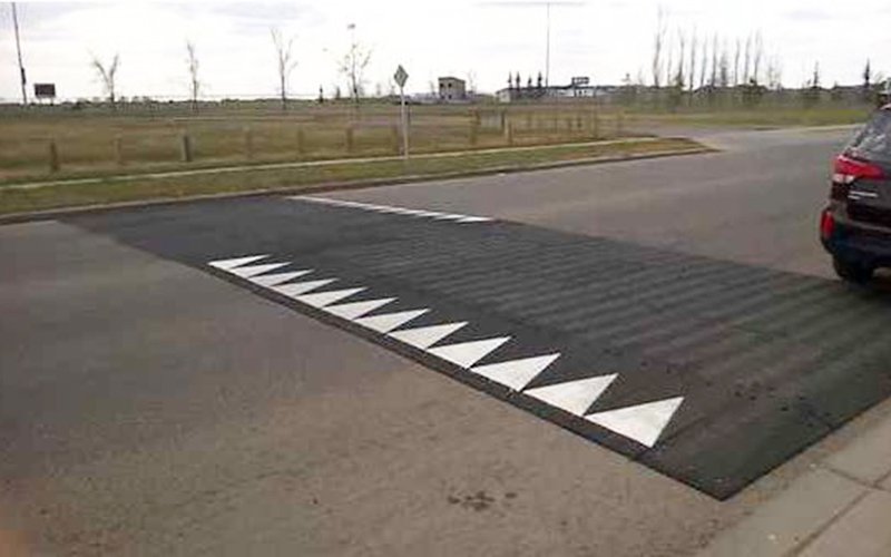 A heavy thick raised rubber flat mat with inclines on edges and spans entire width of road white triangle pointer markings for direction of travel