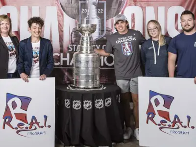 Image of five people standing next to the Stanley Cup holding REAL posters