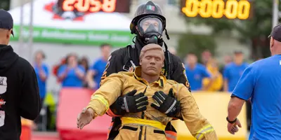 A firefighter supports a rescue-training mannequin dressed in a yellow protective suit.