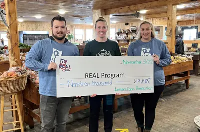 Three people at Lesters Market holding a large cheque written out to the REAL Program