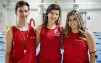 Three lifeguards in red shirts standing in front of a pool