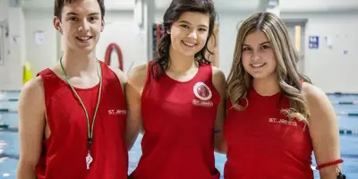 Three lifeguards in red shirts standing in front of a pool