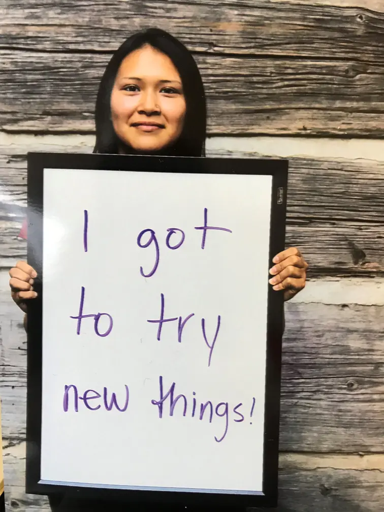 A woman holding a sign that reads "I got to try new things!"